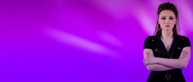 Güçlü ve kendinden emin bir kadın, kollarını kavuşturarak, çarpıcı bir şekilde canlı mor bir arka plana karşı cesurca ayakta duruyor.