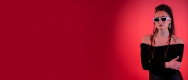 Dengeli bir model şık bir şekilde poz verir, canlı kırmızı bir arka plana karşı cesur moda ve zarafet sergiler.