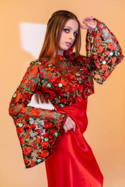 Yetenekli bir manken zarif bir şekilde çiçekli bir bluzu parlak kırmızı bir etekle canlı bir ortamda sergiliyor.