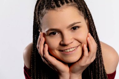 Neşeli genç bir kadın örgülü saçlarıyla mutluluk saçıyor sıcak bir gülümseme ve çekici bir poz sergiliyor..