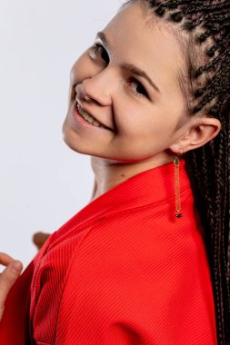 Zarif örgüleri olan kendine güvenen kırmızı elbiseli genç bir kadın neşeyle gülümsüyor, pozitif enerji saçıyor.