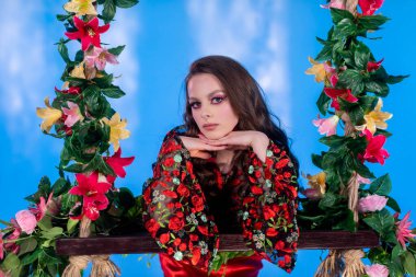 Çarpıcı bir modelin büyüleyici portresi canlı mavi bir arka planda renkli bir çiçekli elbise sergiliyor.