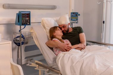 Şefkatli bir hasta, bir hastane yatağında dinlenen küçük bir çocuğu rahatlatır. Yürekten bir bakım anı gösterir.