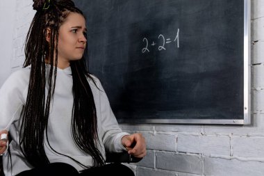 Örgü saçlı bir öğrenci, tahtadaki zor bir matematik problemiyle uğraşırken gözle görülür şekilde endişeli görünür.