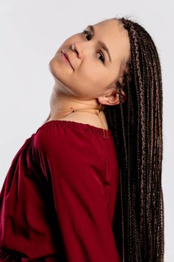 Uzun örgülü saçları olan kendine güvenen bir kadın şık bir kestane rengi elbise içinde poz verir, sofistike ve zarafet saçar.