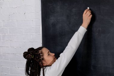 Genç bir öğrenci, öğrenme sürecine olan bağlılığını yaratıcı bir şekilde tahtaya yazmak için hevesle uzanıyor.