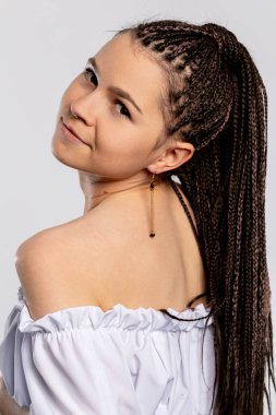 Modayı takip eden genç bir kadın zarif bir şekilde poz veriyor, güzel örgülü saçlarını ve şık dış görünüşünü sergiliyor.