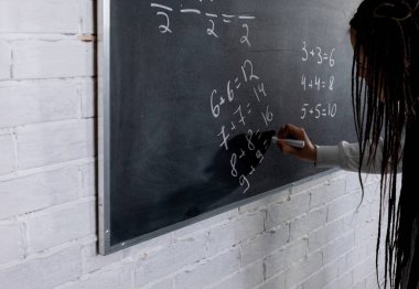 Bir öğretmen, öğrencileri modern bir sınıfa yerleştirirken tahtadaki karmaşık kavramları anlatıyor.