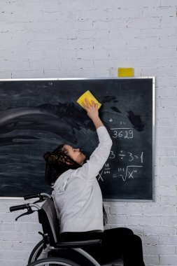 Tekerlekli sandalyedeki biri tahtayı temizler, kararlılığını gösterir ve kapsayıcılık ve erişilebilirliğe bağlılığını gösterir.