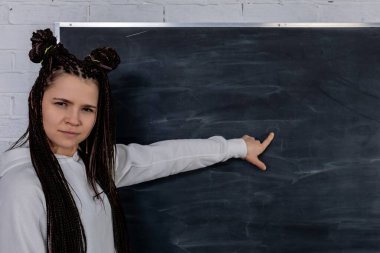 Bir eğitmen güven içinde boş bir tahtaya işaret eder, öğrencileri zenginleştiren bir öğrenme deneyimi için heveslidir.