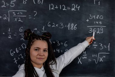 Kendini adamış bir öğretmen, öğrencileri etkin bir şekilde eğitmek için tahtadaki çeşitli matematik problemlerini anlatıyor.