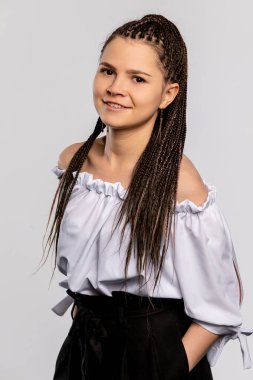 Saçları güzel örülmüş neşeli genç bir kadın şık ve şık bir ofomuz kıyafeti içinde rahatça poz verir.