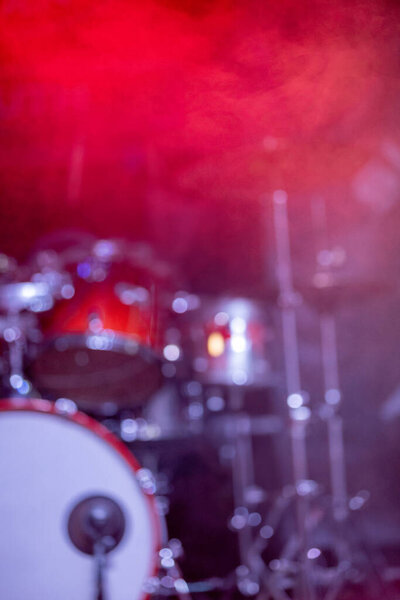 A blurred view of a vibrant drum set lit by colorful stage lights, capturing the energy of a live music event