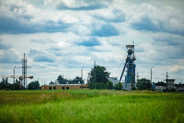 Çeşitli makinelerin sergilendiği sakin bir endüstriyel sahne, yemyeşil alanlar üzerinde geniş bulutlu bir gökyüzü ile birlikte.
