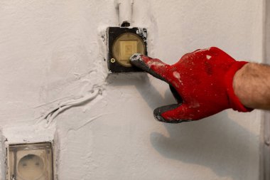 Kırmızı eldivenli bir elektrikçi elektrik sistemi üzerinde çalışırken usta bir şekilde düğmeye basıyor.