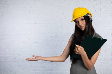 Sert bir şapka takan kendine güvenen bir kadın dik durur ve inşaat işleri için tamamen hazırlanmış çekici bir duruş sergiler.