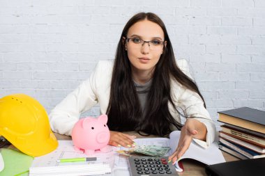 Odaklanmış bir kadın masasında gerekli iş malzemeleriyle çevrili bir hesap makinesi kullanıyor.