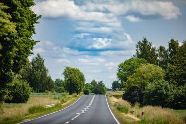 Bereketli ağaçlar ve canlı bulutlarla kaplı manzaralı bir köy yolu seyahat görüntüsü ve ilham için mükemmel.
