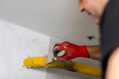 Bir kişinin detaylı bir yakın çekimi ustalıkla bir fırça aracı kullanarak canlı sarı boya ile bir duvar boyama