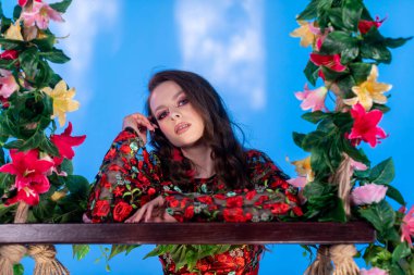 Canlı çiçekler ve yeşillikler arasında bir modelin portresi, cesur ve yenilikçi moda ifadeleri sergiliyor.