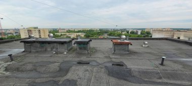 Kentsel bir çatı manzarası bacalarla süslenmiş ve şehrin genişleyen bir silüeti var.