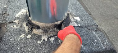 Bir insan çatıda bulunan metal bir direğin tabanında bakım görevlerini dikkatle yerine getirir.