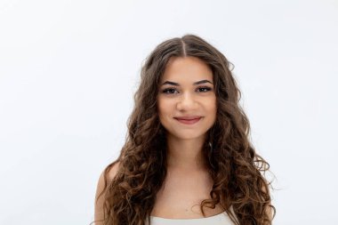 Güzel kıvırcık saçlı neşeli ve hayat dolu genç bir kadın zarif bir poz verir.