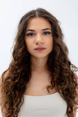 Güzel kıvırcık saçlı genç bir kadın minimalist bir ortamda kendine güvenini ve zarafetini sergiliyor.