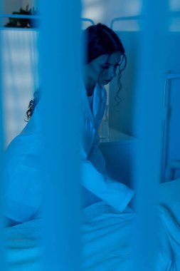 Bir sağlık çalışanı, sakin, mavi bir ortamda hastayla kibarca etkileşime geçer ve onların şefkat ve şefkatini vurgular.