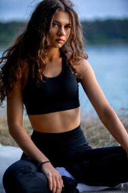 Yoga kıyafetli, huzurlu ve rahatlatıcı bir görüntü. Huzurlu bir gölün yanında derin derin meditasyon yapan bir kadın.