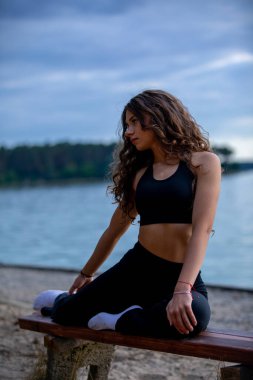 Genç bir kadın plajda yoga yapıyor. Huzur, zindelik ve huzur dolu su ile uyum sağlıyor.