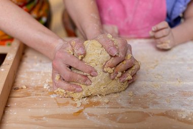 Kaba ahşap bir yüzey üzerinde çoklu ellerin hamur yoğurduğu enfes bir iş birliği anı.