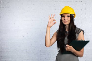 İnşaat kaskı takmış bir kadın elinde bir panoyla profesyonelliği vurguluyor..