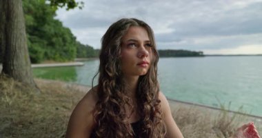 Huzurlu göl kıyısında huzur içinde oturan genç bir kadın doğanın sükunetini ve güzelliğini derinden kucaklıyor.