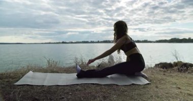 Genç bir kadın, huzur dolu bir gölün kenarında yoga pozu veriyor. Güzellik ve sağlığın faydalarını kucaklıyor.