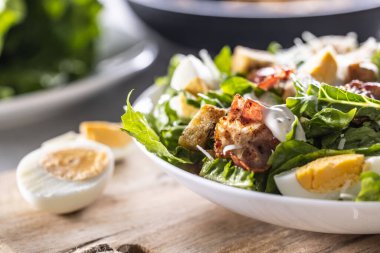 Beyaz bir kase dolusu kızarmış ekmek, domuz pastırması ve parmesan peynirli Cezar salatası..