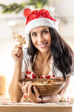 Noel önlüğü giymiş genç bir esmer bir kase dolusu zencefilli ekmek pişirmiş, onlardan birini elinde tutuyor, işinden memnun..