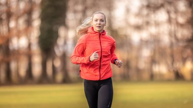 Spor giyimli güzel bir sarışın parkta koşmak için antrenman yapıyor..