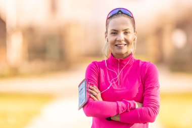 Spor kıyafetli güzel bir sarışının portresi, koşmaya hazır, kulaklıkla müzik dinliyor..