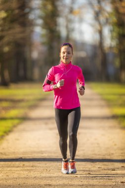 Spor giyimli güzel bir sarışın parkta koşmak için antrenman yapıyor..
