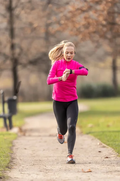 stock image Young woman runner checks her smart watch while running in the park.