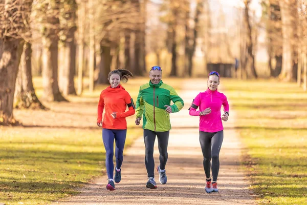 stock image A trio of runners, two young women and one mature man are running in an autumn park.