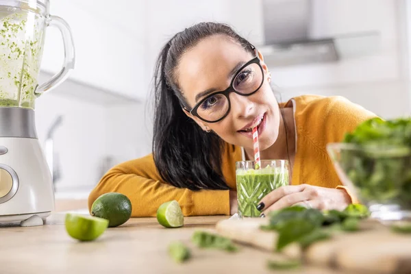 A funny young woman drinks a green smoothie that she made herself. Concept of healthy lifestyle and eating.
