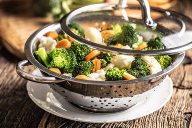 Steamed broccoli, carrots and cauliflower in a stainless steel steamer with a lid. Healthy vegetable concept.