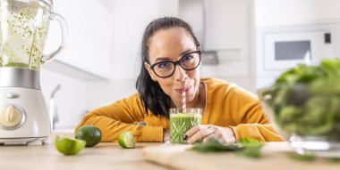 A funny young woman drinks a green smoothie that she made herself. Concept of healthy lifestyle and eating.