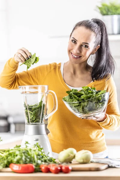 Smiling woman making spinach smoothie, putting leaves in blender. Concept of healthy lifestyle and eating.