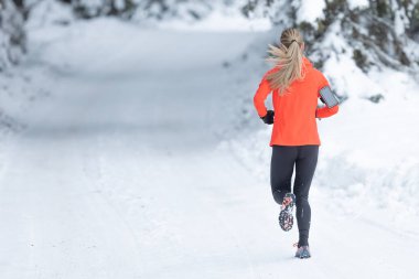 Running in winter, rear view of a female runner on a snowy path in a park or forest.