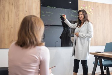 Two female office colleagues are working on a joint project. They consult a joint project on the blackboard.