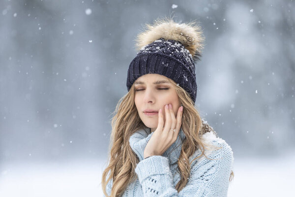 A young woman has a toothache outside in winter weather, she has sensitive enamel to the cold.
