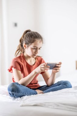 Genç bağımlı oyuncu kız evde bir yatakta otururken telefonla oynuyor.. 